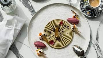 Prato de sobremesa com design espiral, decorado com flores comestíveis e frutas vermelhas, sobre uma mesa de mármore.