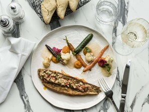 Une assiette contenant un poisson grillé, garni de tomates coupées en dés et d’herbes aromatiques, accompagnée de légumes et de pain.
