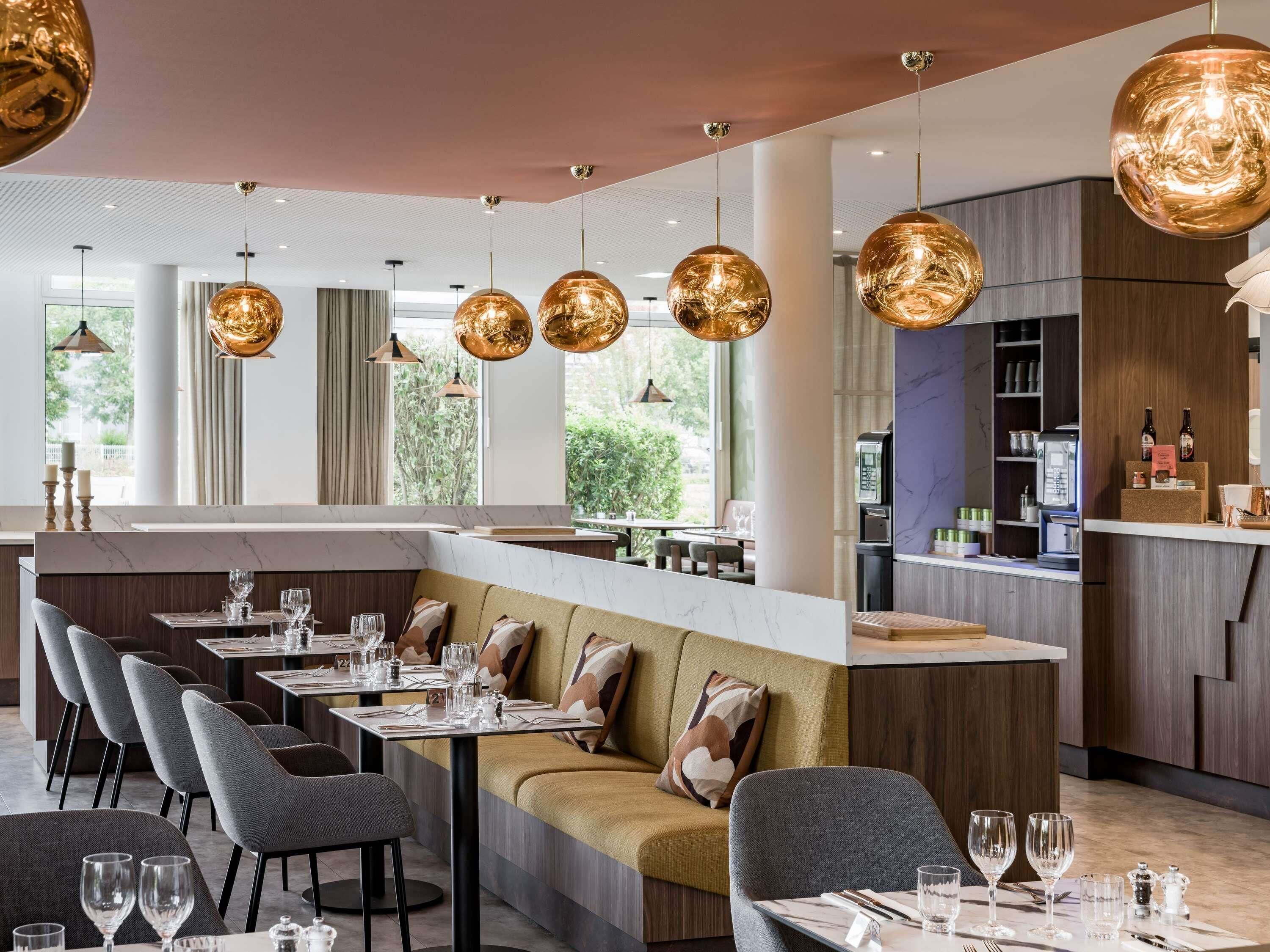 Un restaurante moderno con una barra larga, varias zonas de estar e iluminación colgante.