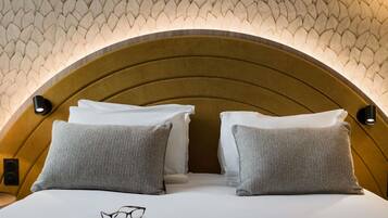 A neatly made bed with white linens, two grey pillows, and a pair of glasses on the bed.