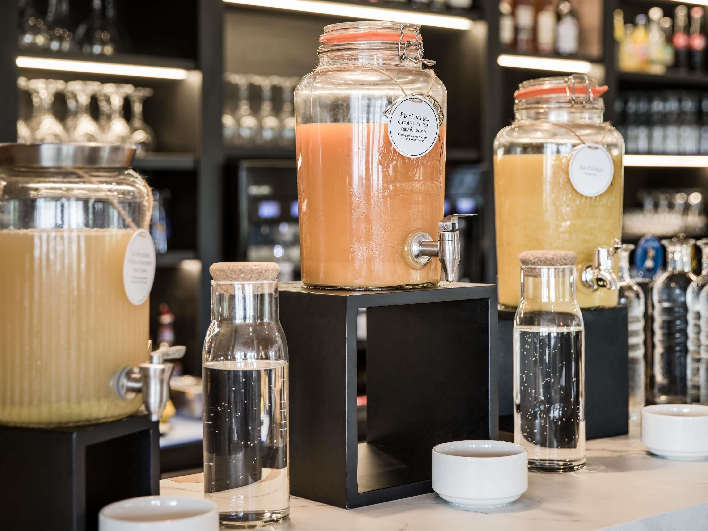 A beverage station with multiple dispensers and containers, including a large orange-colored drink and smaller bottles.