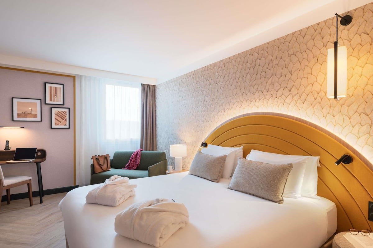 A hotel room with a large bed, a desk with a laptop, a chair, and a sofa.