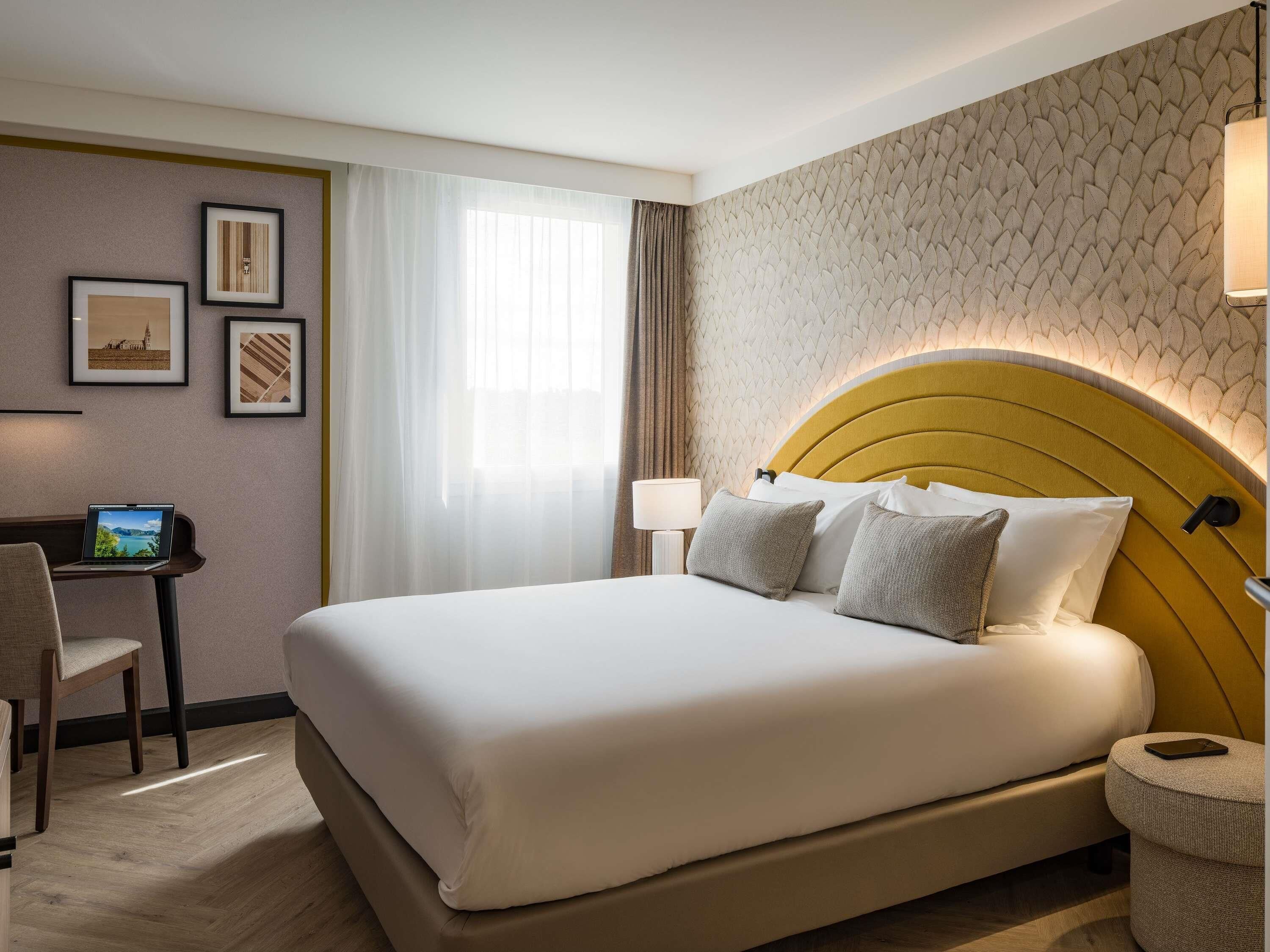 A hotel room with a large bed, a desk with a laptop, and a chair.