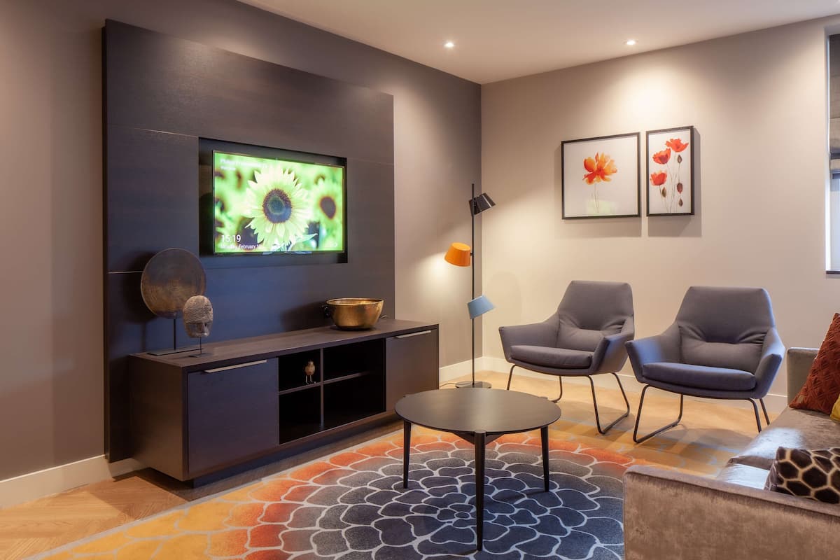 Un soggiorno moderno con una TV a schermo piatto, due poltrone grigie, un tavolino da caffè, un consolle con oggetti decorativi e quadri appesi alla parete.
