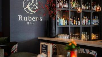 Een bar genaamd Rubens BAR met planken vol drankflessen en een decoratieve vaas met rode bessen.