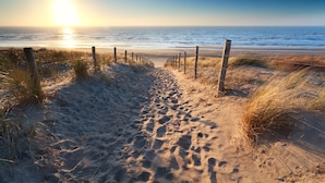 A sandy beach path leading to the ocean with a wooden fence.