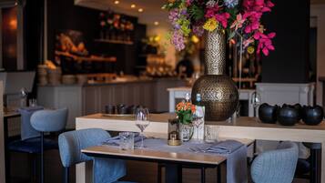L’intérieur d’un restaurant, avec un espace bar, des tables et des chaises, et un vase décoratif rempli de fleurs.