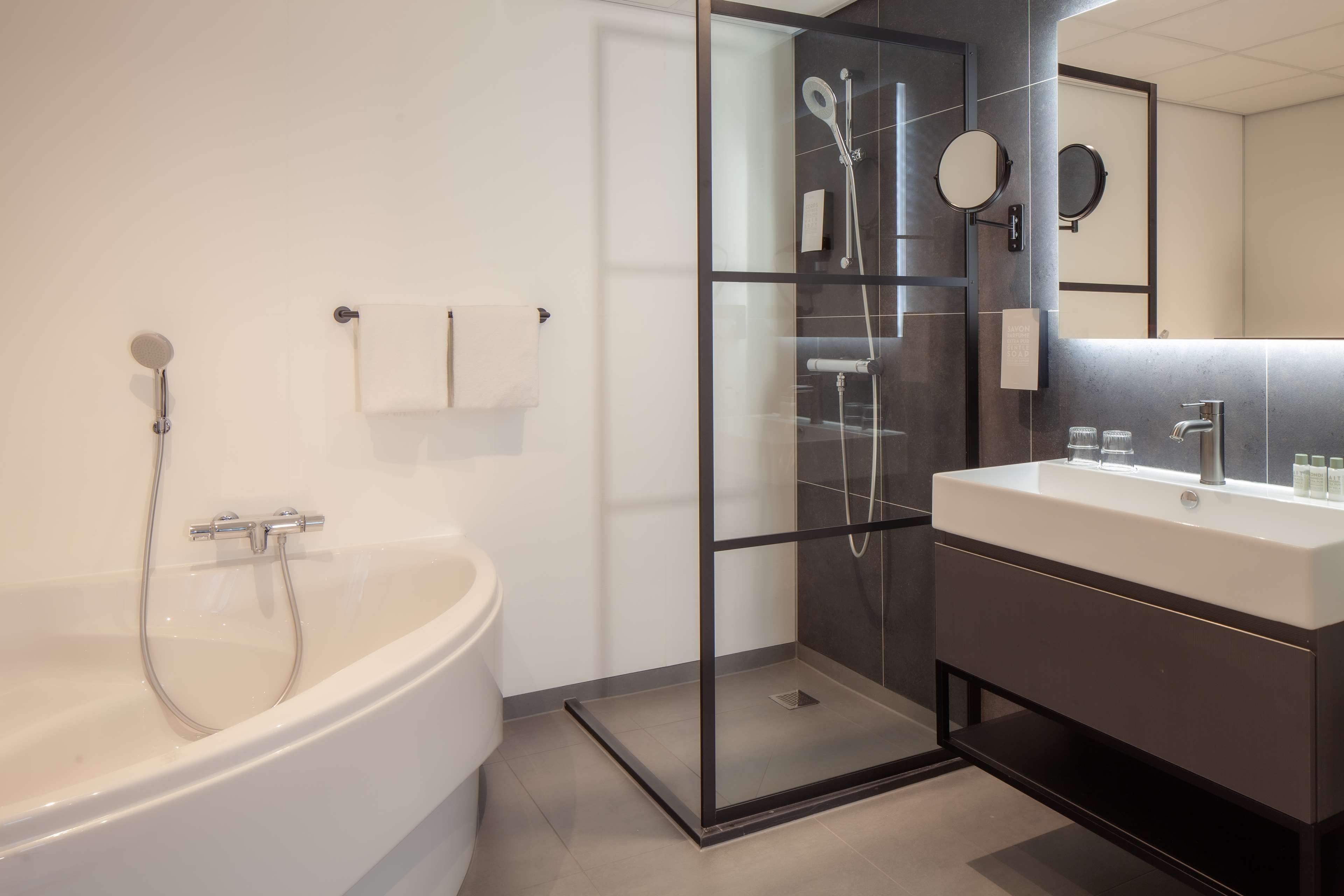 Un baño moderno con una bañera independiente, cabina de ducha con mampara de vidrio y tocador con espejo.