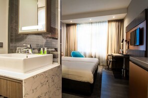 A hotel room with a marble bathroom sink, a bed, a desk, a chair, a TV mounted on the wall, and a window with curtains. - Golden Tulip Leiden Centre (Leiden)