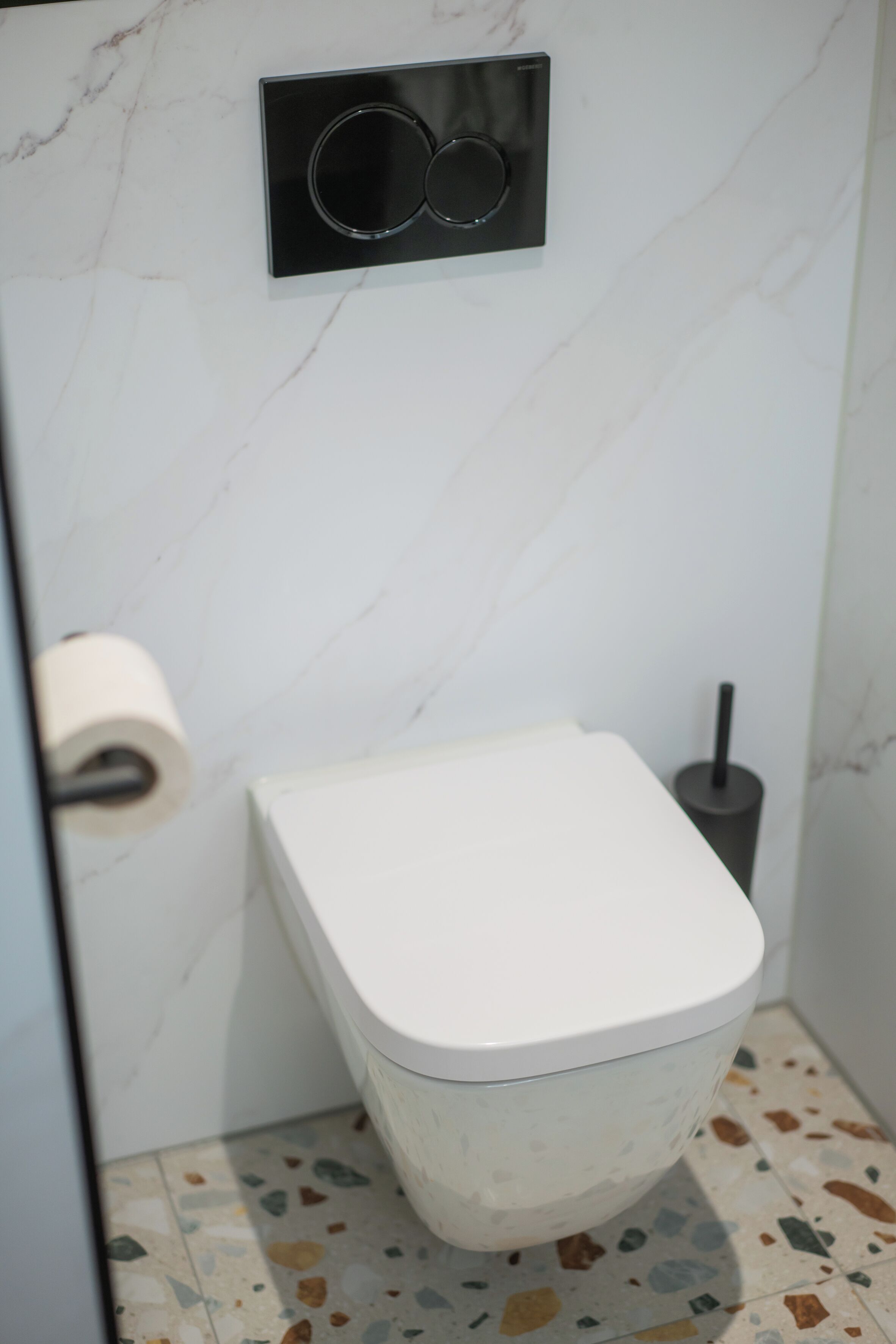 A bathroom with a white toilet, a marble wall, and a toilet paper holder.