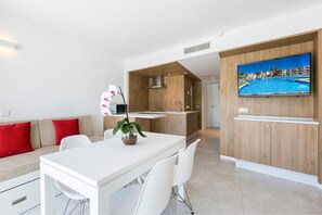 Een moderne keuken met houten kasten, een witte eethoek en een tv aan de muur met een afbeelding van een zwembad.