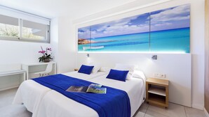 Een moderne slaapkamer met een groot bed, een bureau en een wanddecoratie van een strandgezicht.