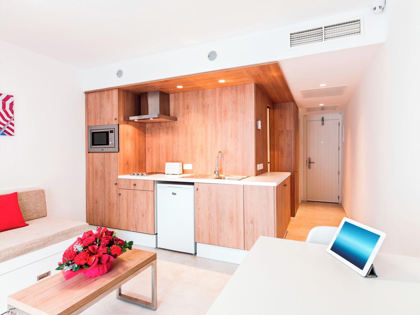Una cocina moderna con armarios de madera, microondas integrado y lavavajillas. Hay una zona de comedor con una mesa y un ramo de flores.