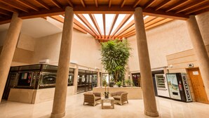 Een ruime lobby met een hoge plafond, grote zuilen en een centraal gelegen zithoek met een plant.
