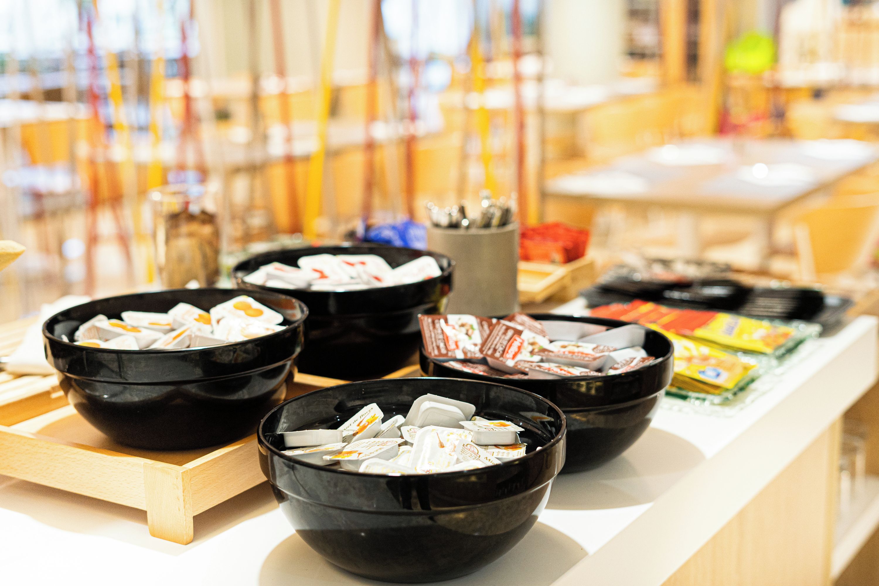 A buffet with multiple black bowls containing various food items, a wooden serving tray, and a counter with packaged goods.