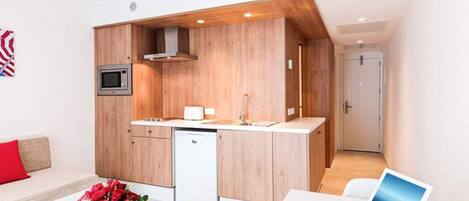 Una cocina moderna con armarios de madera, un microondas integrado y un lavavajillas. Hay un pequeño comedor con una mesa blanca y un cojín rojo.