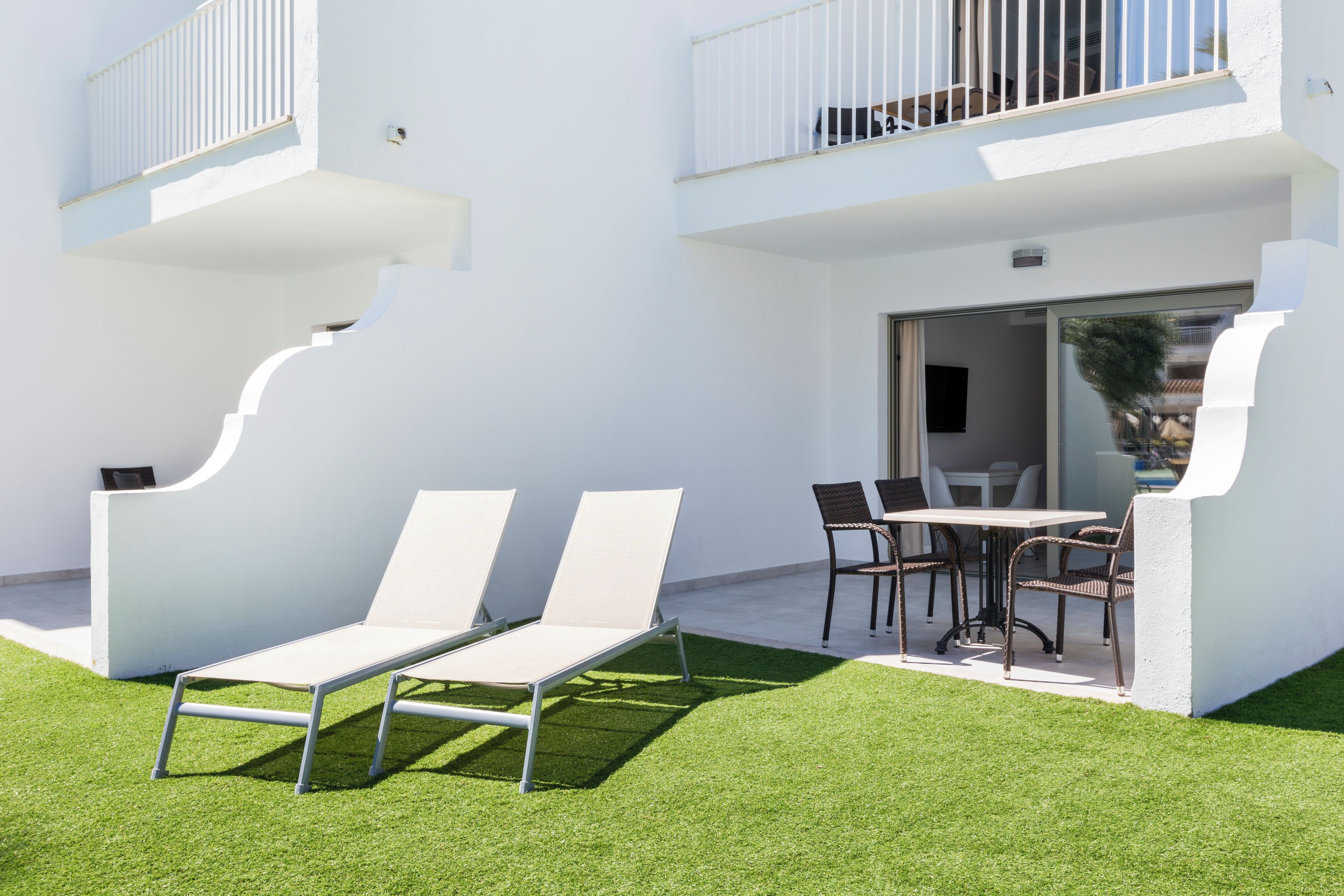 A modern outdoor patio with white lounge chairs, a dining table, and wicker chairs.