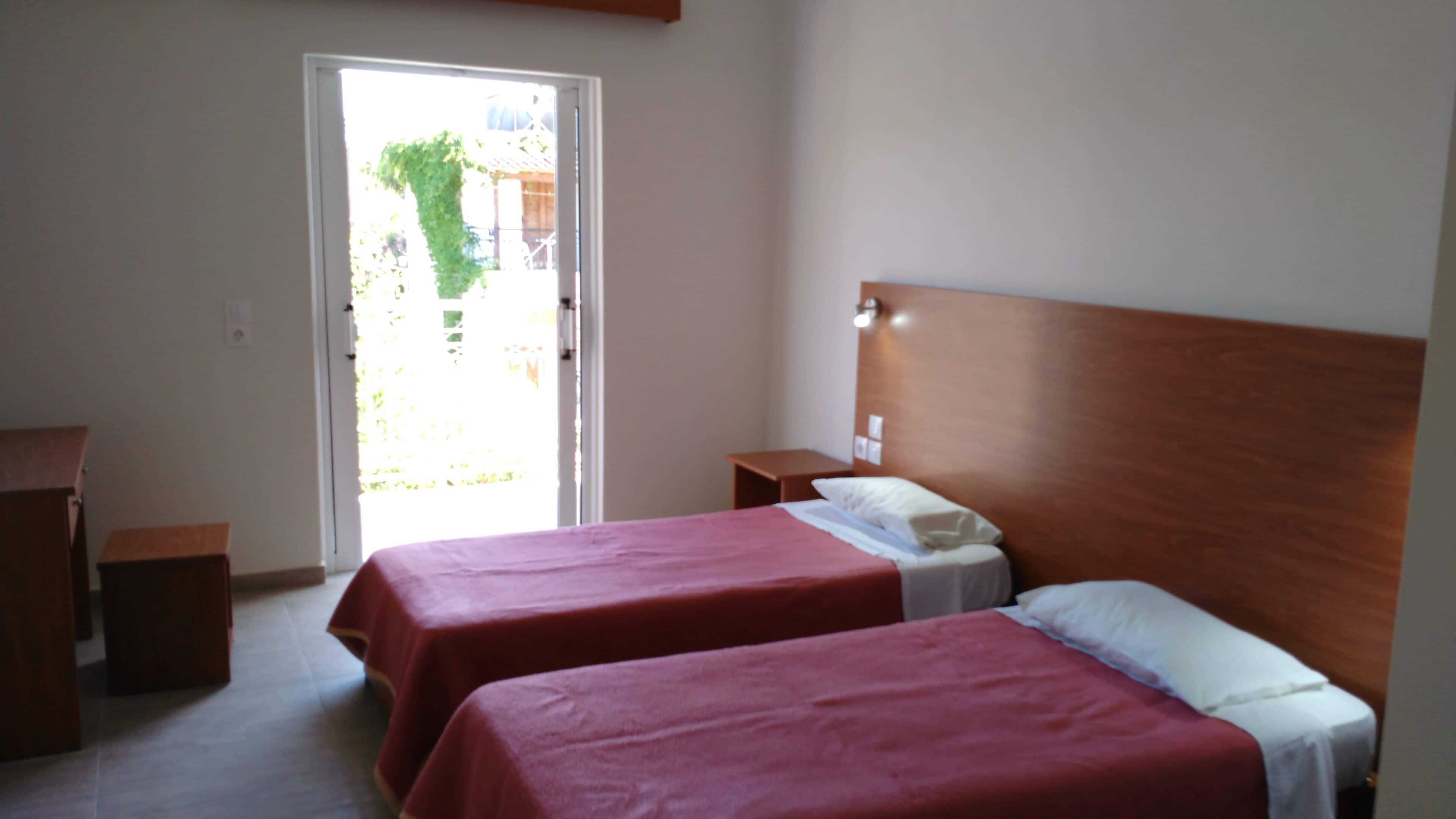 A room with two beds, a wooden headboard, a small bedside table, and a door leading outside.