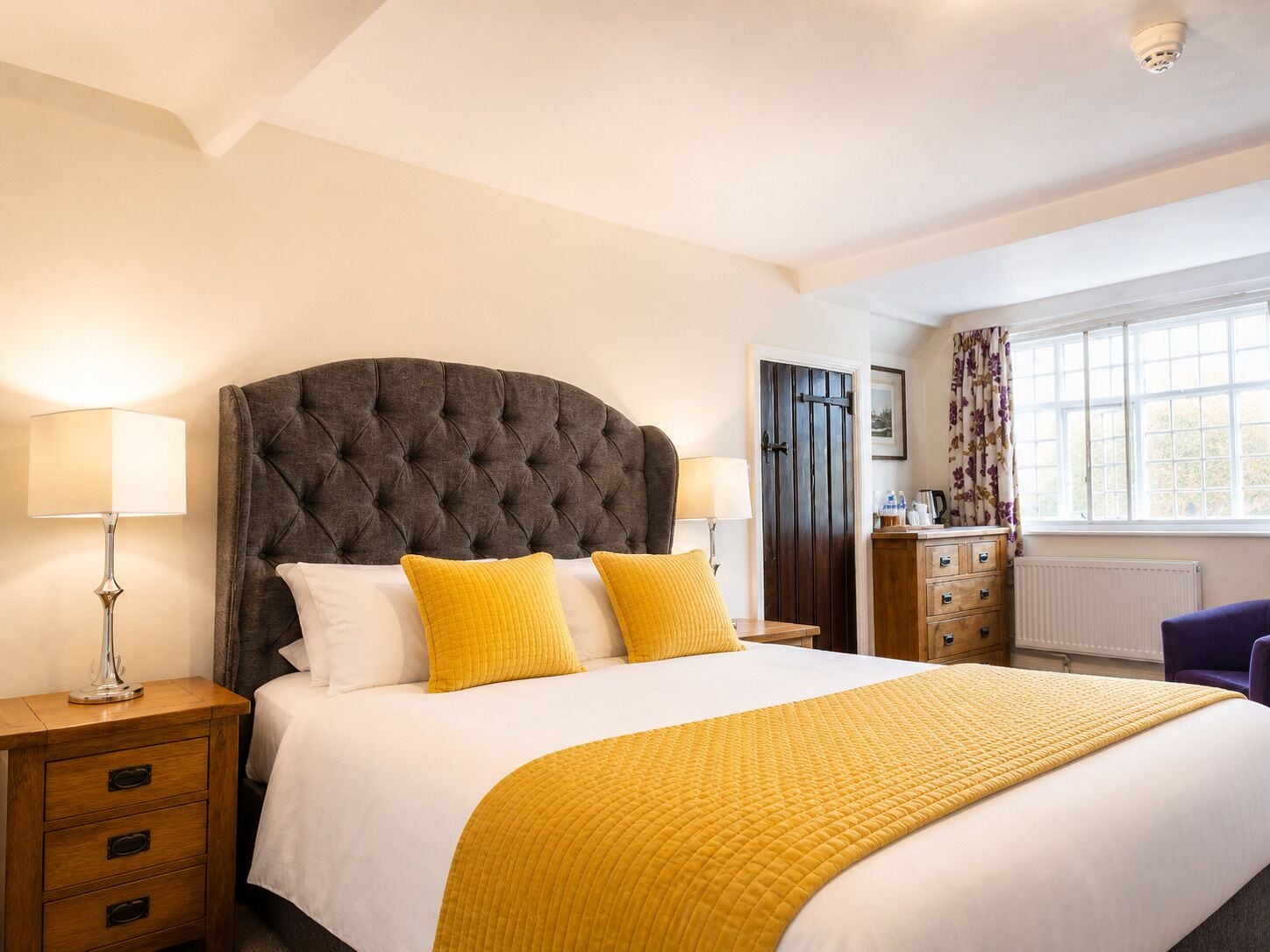 A bedroom with a large bed, two bedside tables, a dresser, and a window with curtains.