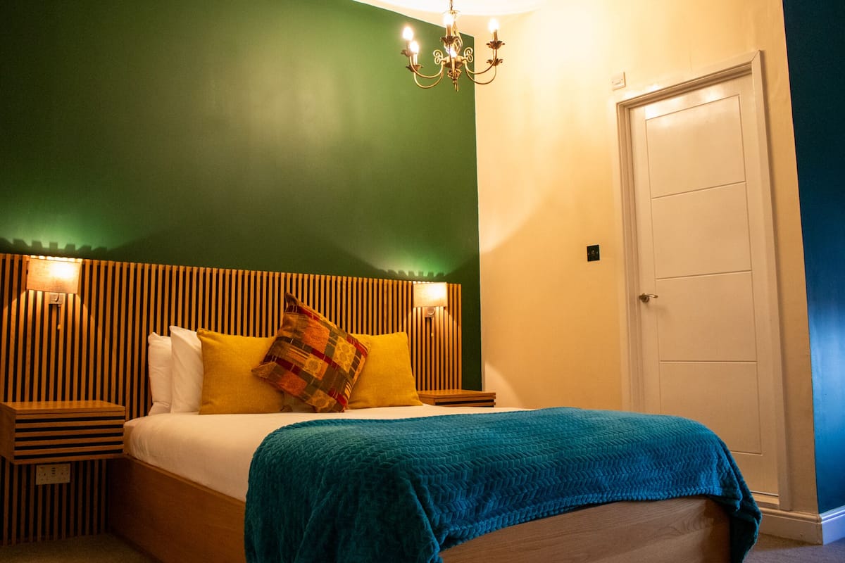A bedroom with a bed, wooden headboard, two bedside tables, a nightstand, a door, and a chandelier.