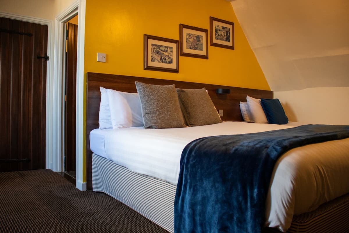 A hotel room with a large bed, a wooden headboard, and three framed pictures on the wall.