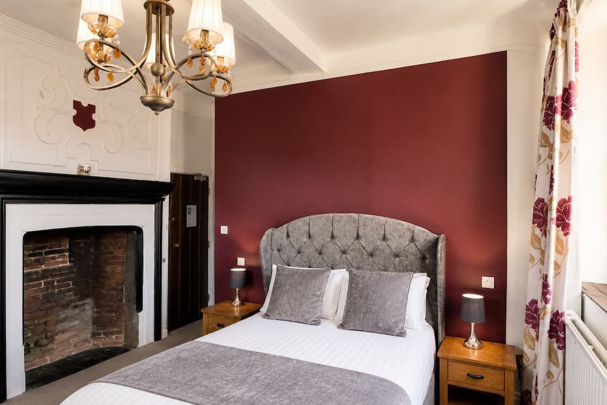 A bedroom with a tufted headboard, a fireplace, two bedside tables with lamps, and a floral curtain.