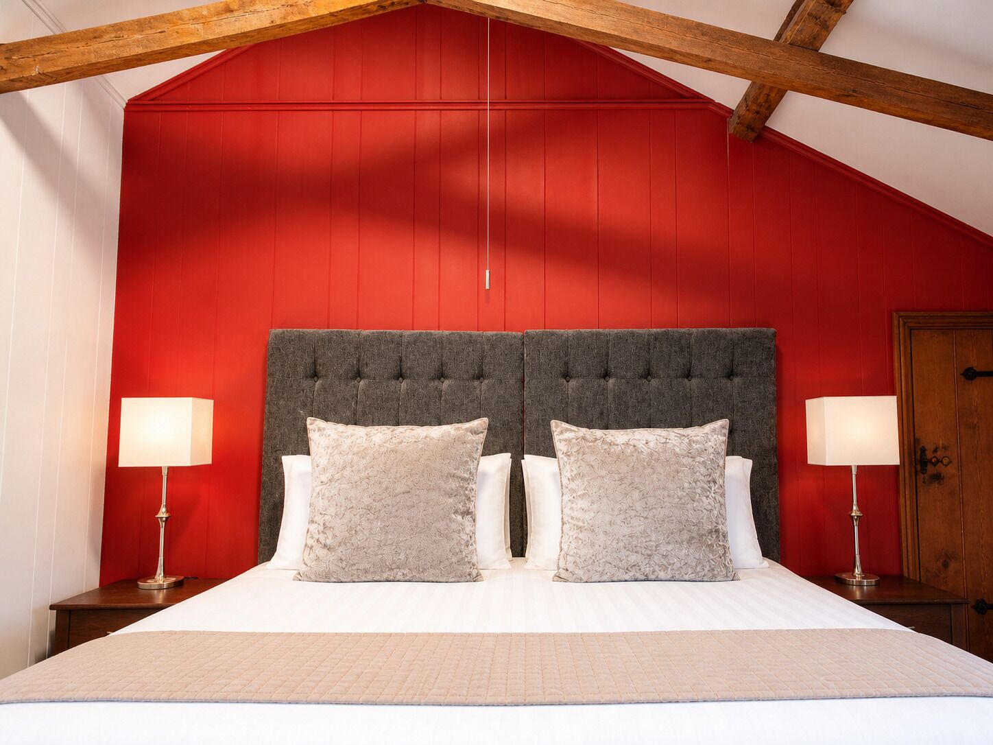 Quarto com parede vermelha, cabeceira estofada, duas luminárias de cabeceira e cama com roupa de cama branca.