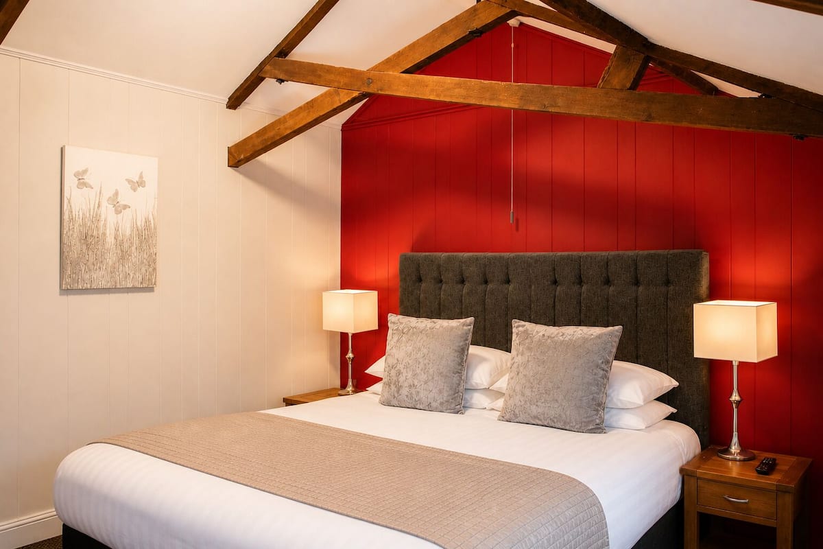 A bedroom with a red wall, a tufted headboard, a bed with white linens, two bedside tables with lamps, and a painting on the wall.