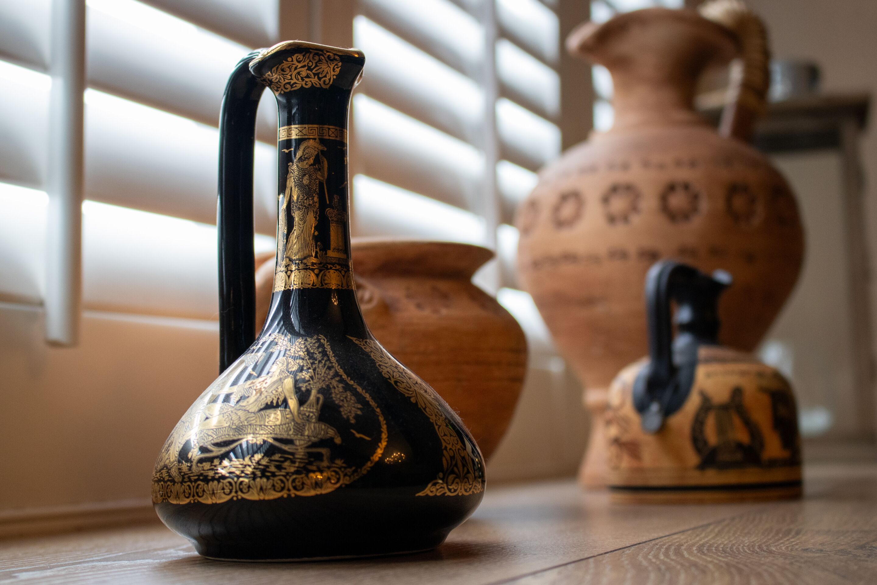 A black and gold vase with a narrow neck and a wide base, placed on a wooden floor.