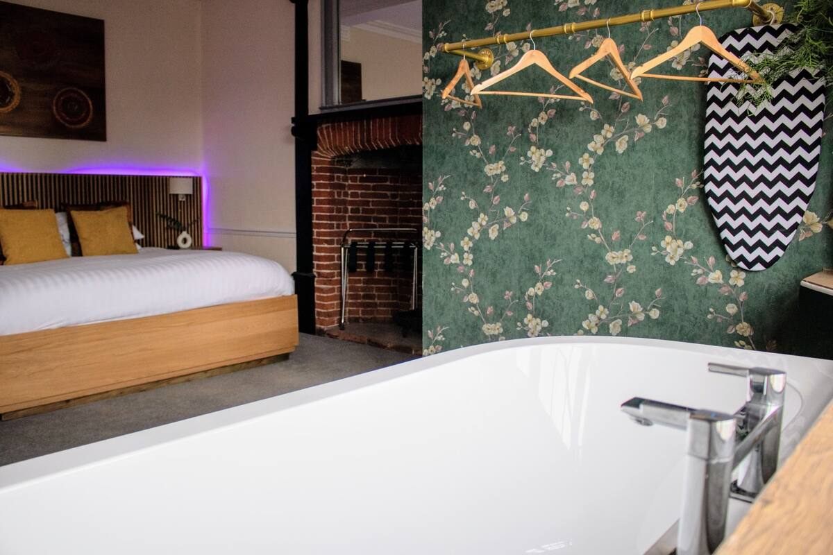 A modern bedroom with a large bed, a brick fireplace, and a bathroom with a white bathtub and wooden accessories.