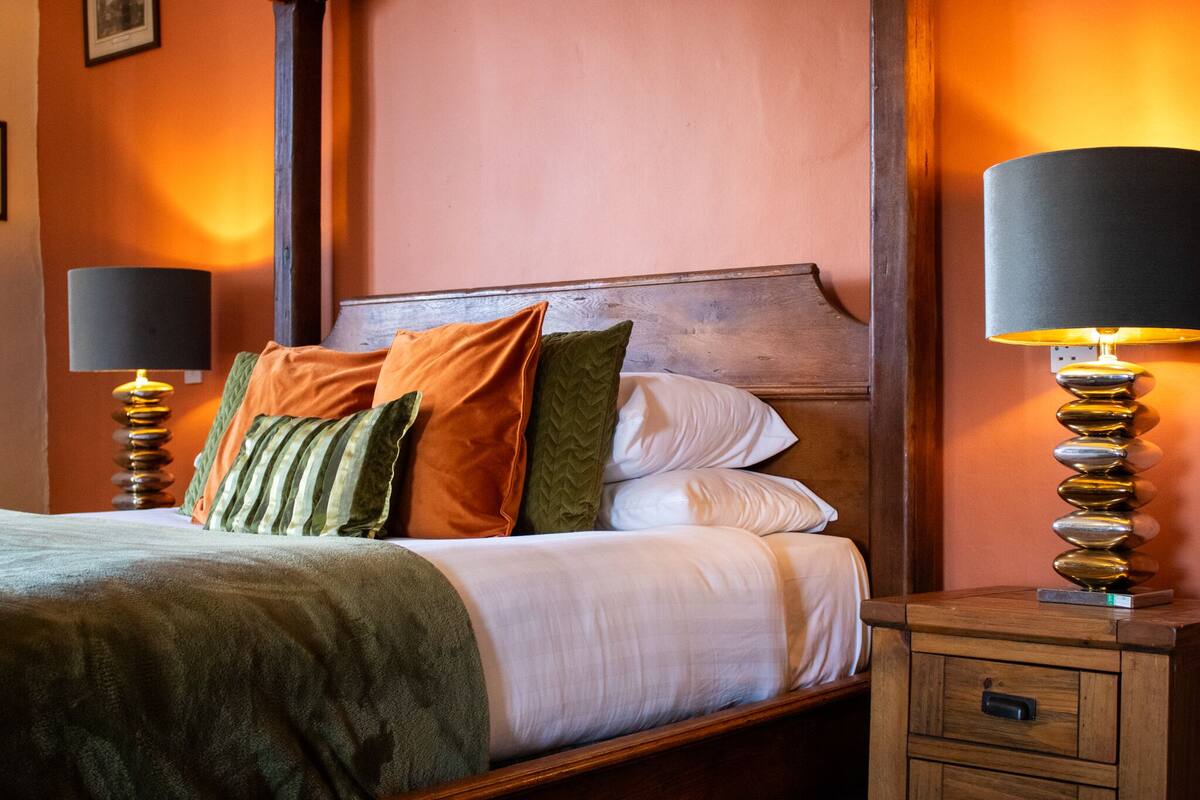 A neatly made bed with a wooden headboard, flanked by two bedside tables with lamps, in a room with orange walls.
