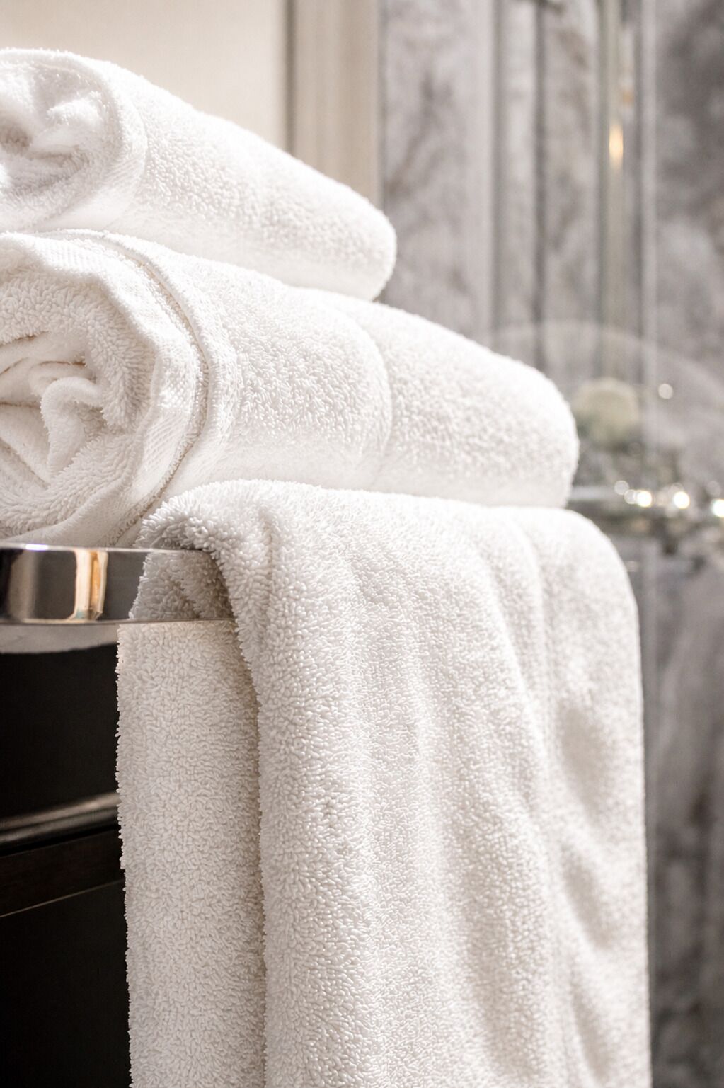 Une pile de serviettes blanches est posée sur une surface métallique, probablement dans une salle de bain.