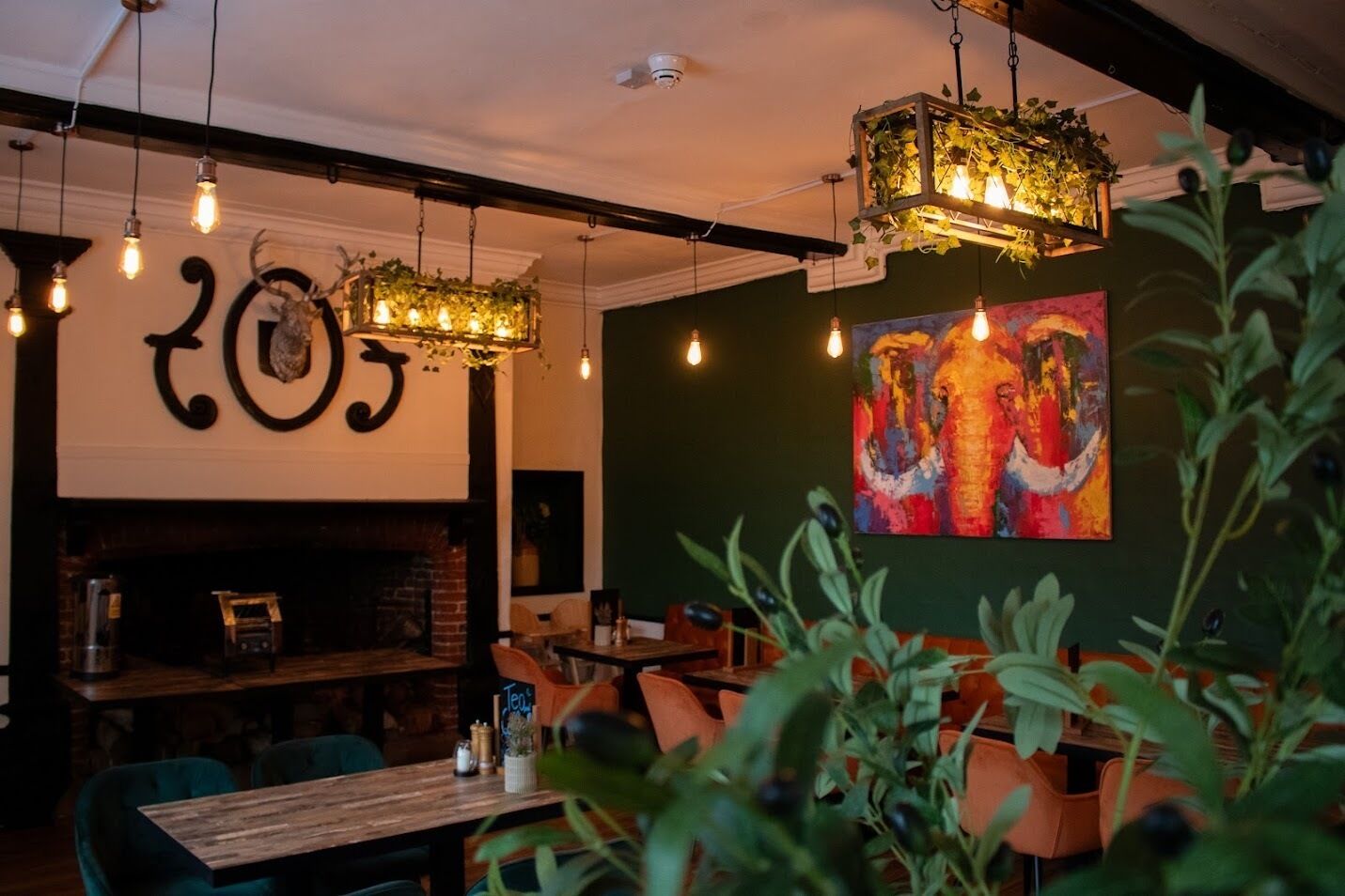 Interior de restaurante con lámparas colgantes, chimenea y un cuadro en la pared.