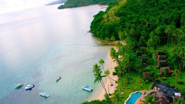 Una playa tropical con varios barcos, una piscina y abundante vegetación.