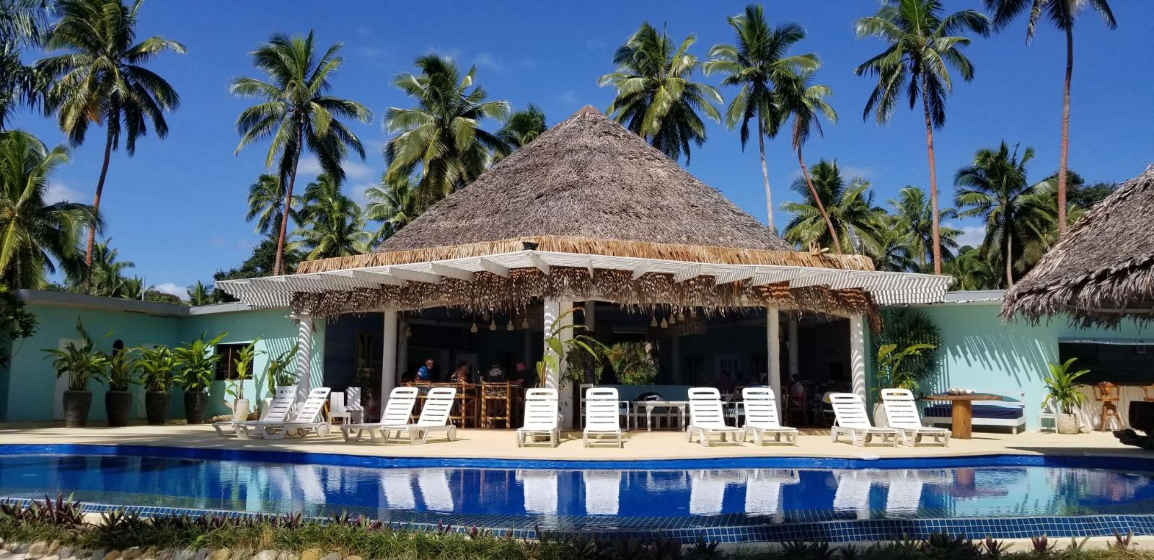 A poolside area with lounge chairs, a thatched-roof pavilion, and palm trees.