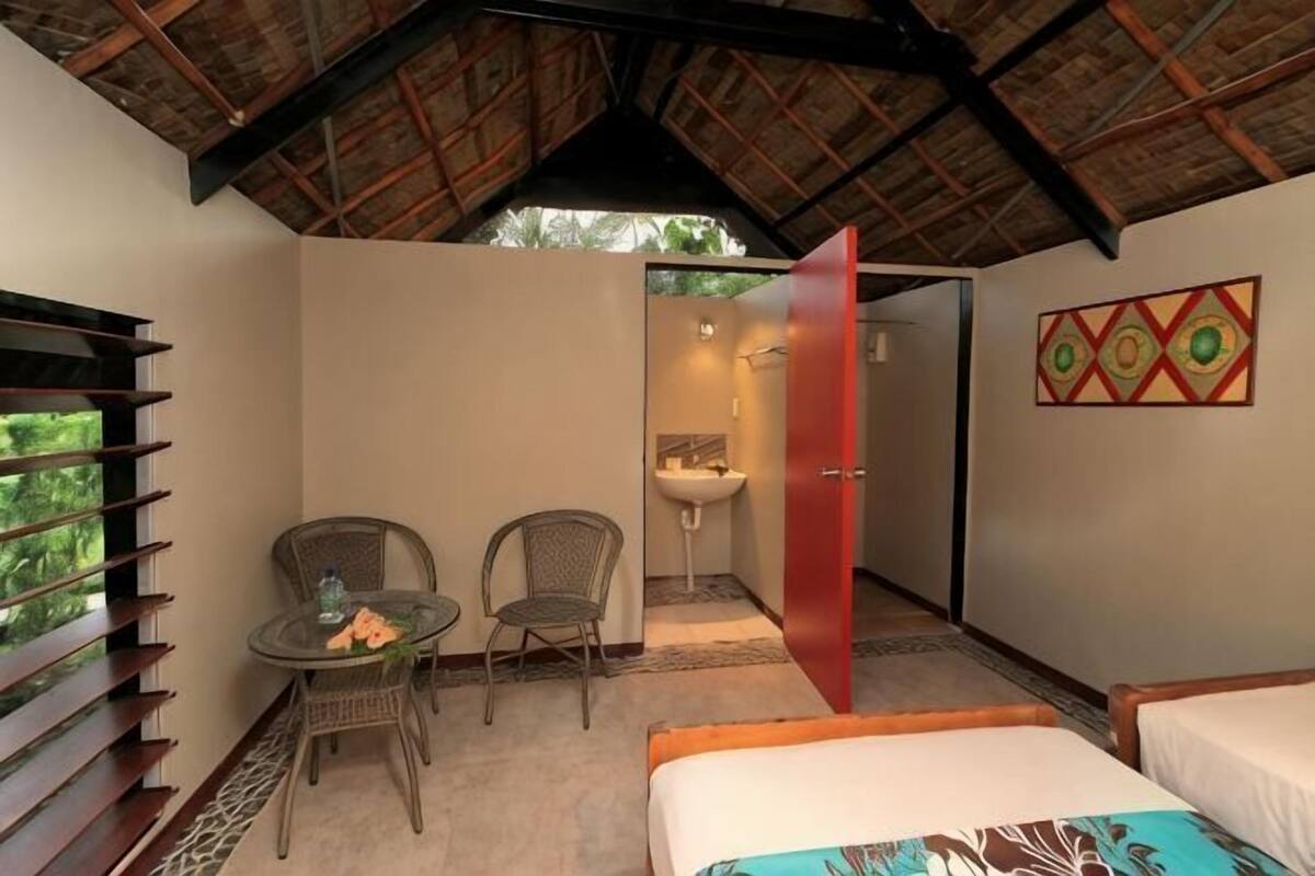 A room with a bed, two chairs, a small table, a sink, and a door leading to another room.
