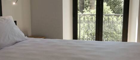 A bedroom with a bed, a wall-mounted light, and a window with a view of trees.