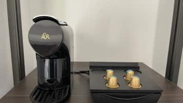 A black coffee maker with a gold logo on the lid, placed on a wooden table next to a black box with four gold-colored knobs.