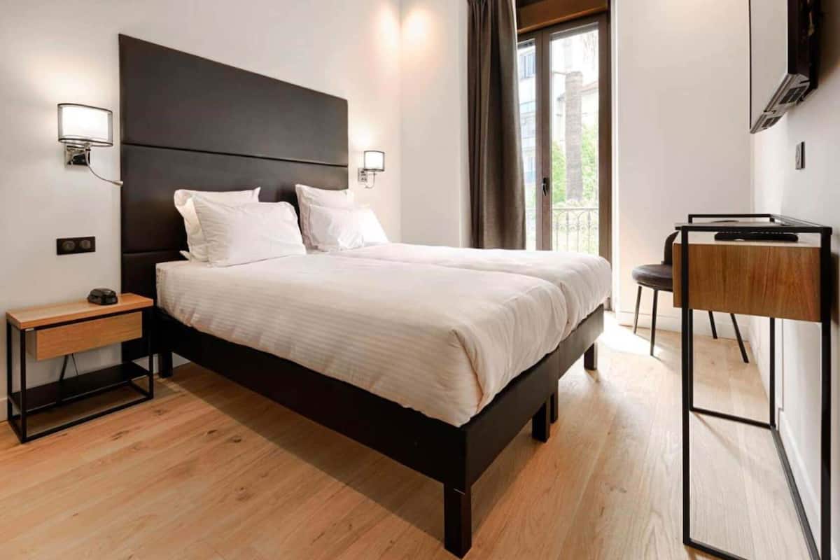 Ein modernes Schlafzimmer mit einem großen Bett, Nachttischen, einem Schreibtisch und einem Fernseher.