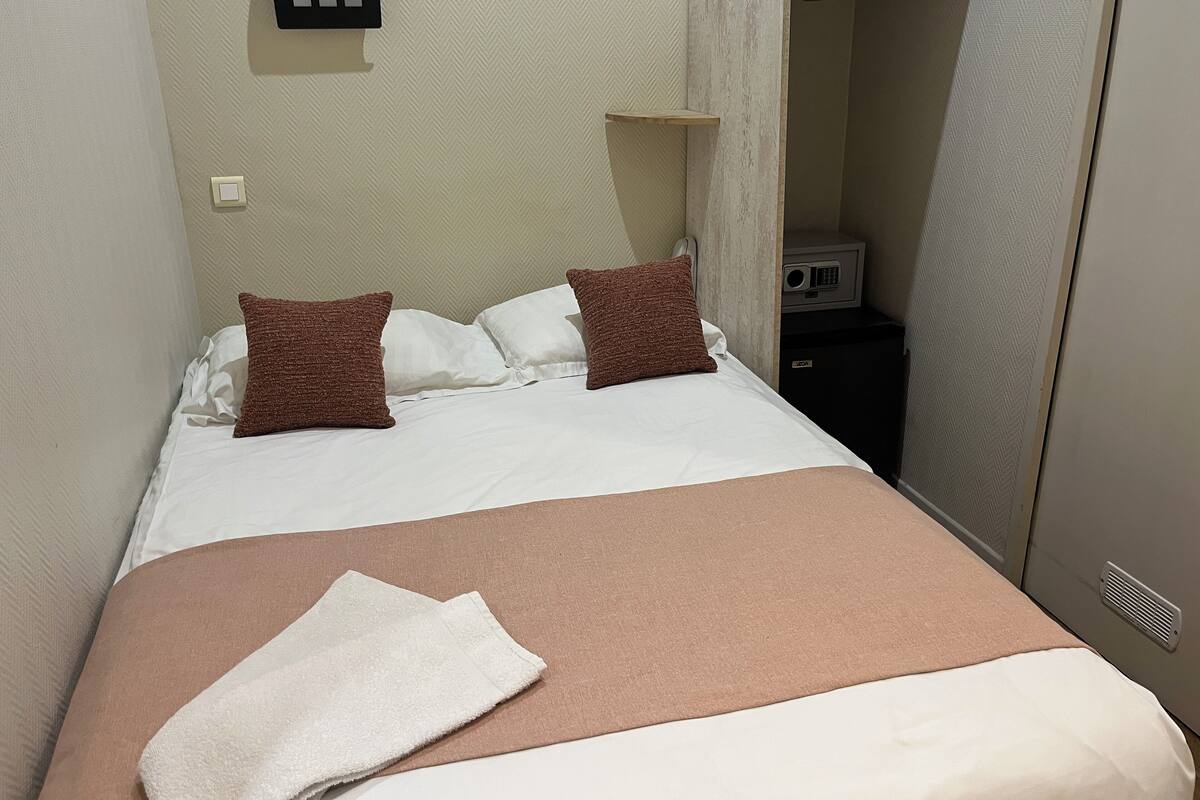 A neatly made bed with a brown and white bedspread, two brown pillows, and a white towel.