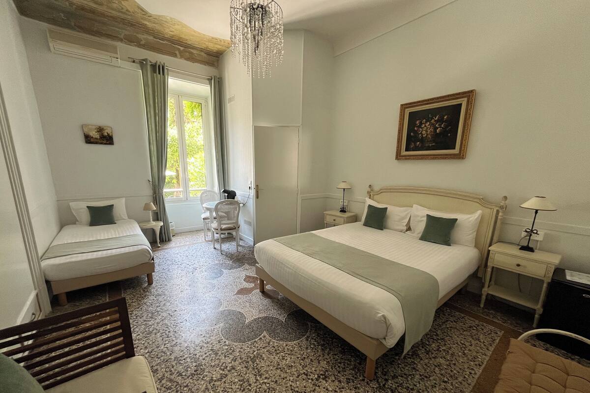 A hotel room with a large bed, a smaller bed, a desk, a chair, and a chandelier.
