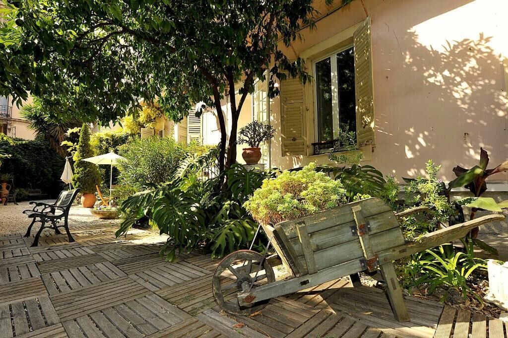 Terrassa exterior amb un banc de fusta, una carreta i plantes en testos.