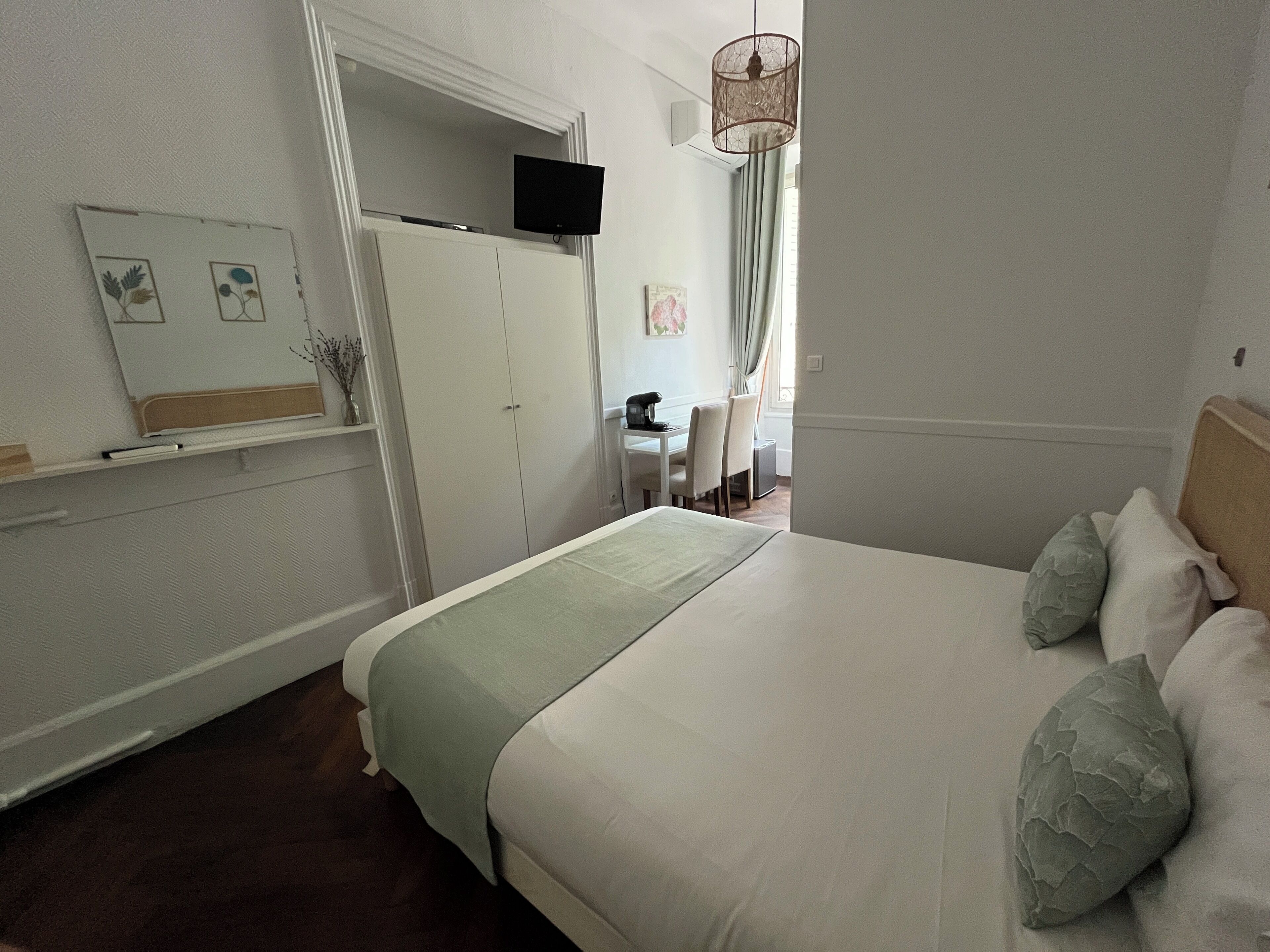 A bedroom with a bed, a desk, a chair, a television, and a window with curtains.