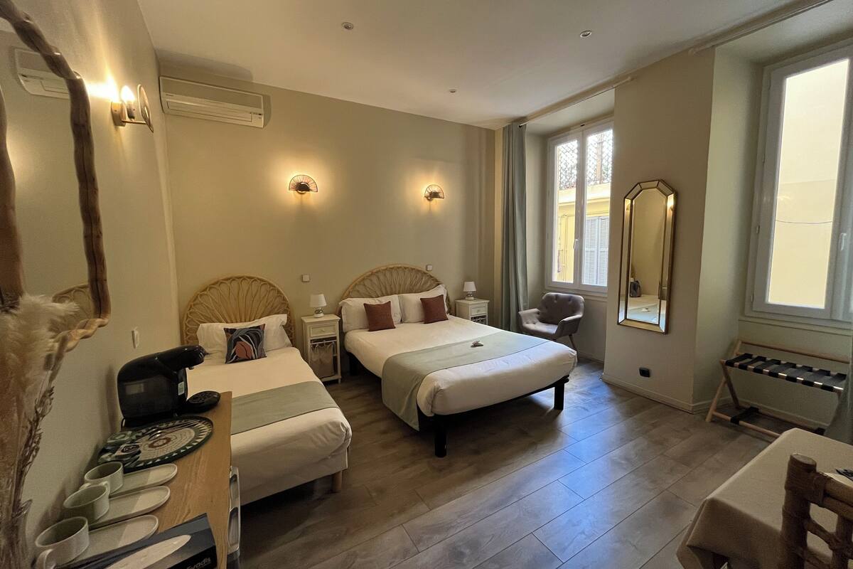 A hotel room with two beds, a desk, a chair, a mirror, and a window.