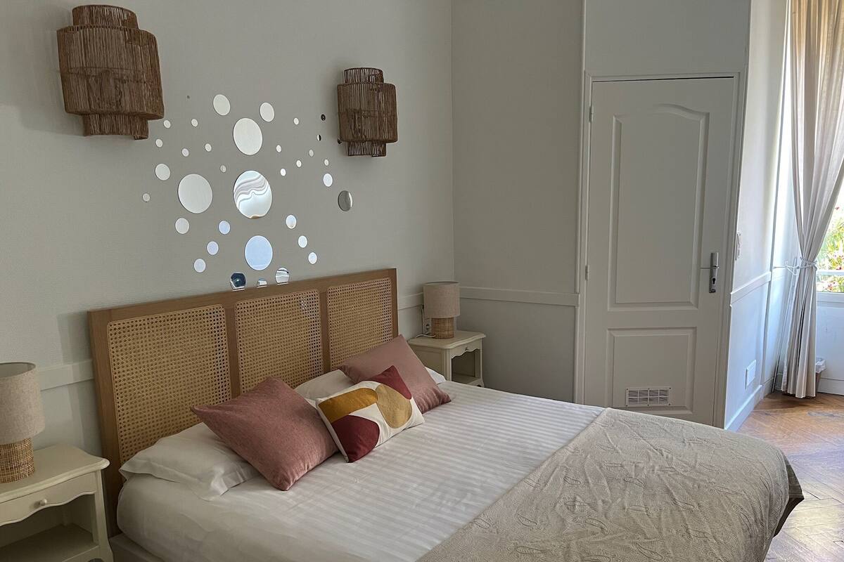 A bedroom with a bed, a nightstand, a lamp, a door, and a wall decoration.