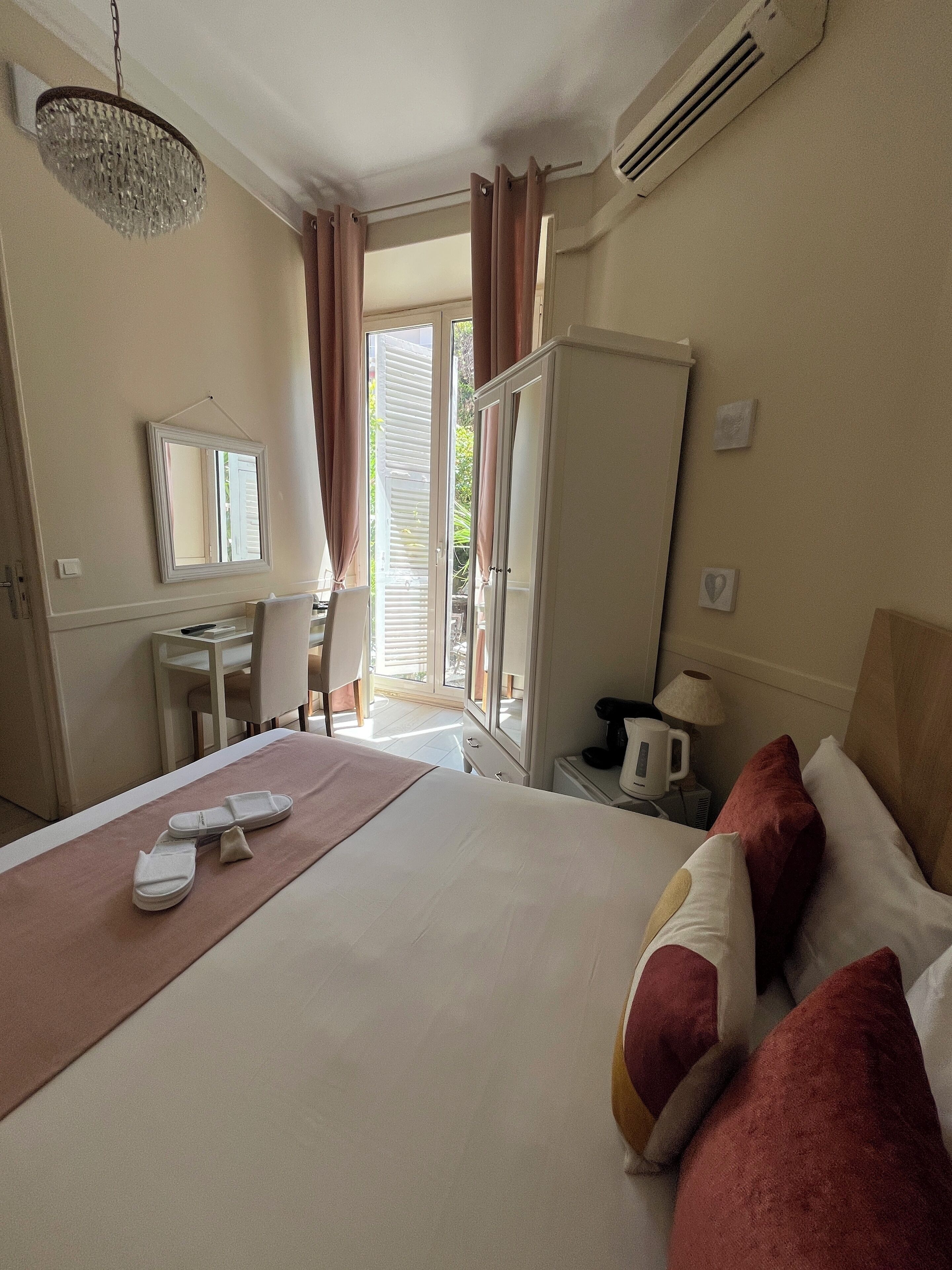A hotel room with a bed, a desk, a chair, a mirror, a wardrobe, and a window with curtains.