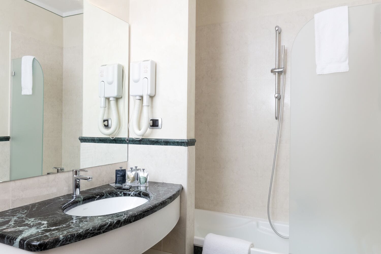 A modern bathroom with a marble sink, a large mirror, two hand dryers, and a shower.