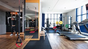 A modern gym with exercise equipment, a mirror, and large windows. - Garda Hotel (Montichiari)