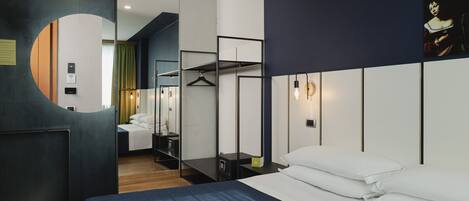 Una habitación de hotel moderna con una cama grande, un armario, un espejo y una lámpara colgante.