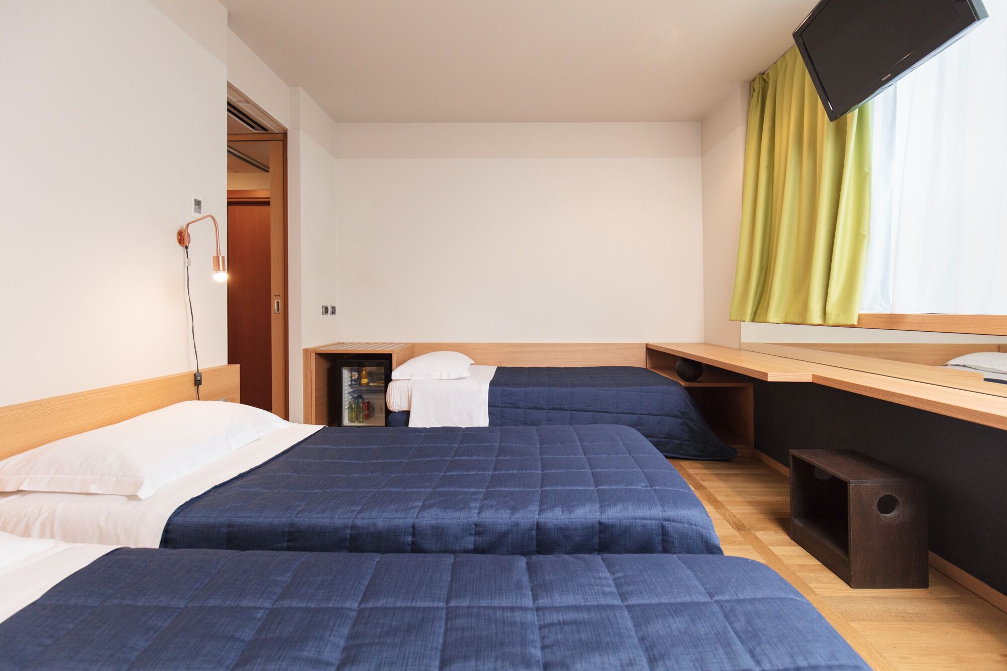 Ein Hotelzimmer mit zwei Betten, einem kleinen Schreibtisch, einem Fernseher und einem Minikühlschrank.